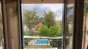 Vista a través de un ventanal a un patio exterior con piscina, mobiliario de madera y una mesa.