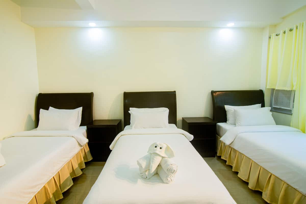 A hotel room with three single beds, each with a dark headboard and white bedding.