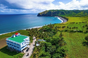 Un hotel frente al mar con techo verde, varios pisos y vistas al océano y las colinas.