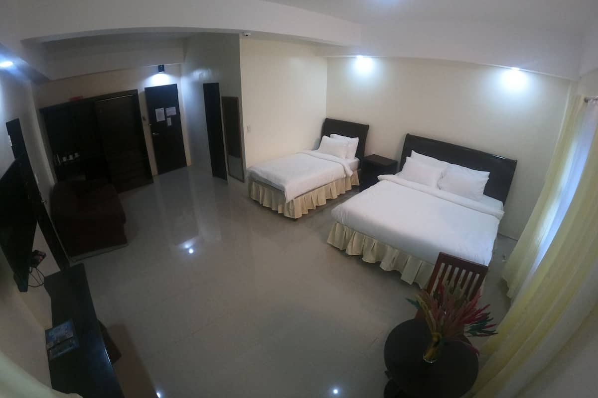 A hotel room with two beds, a desk, and a chair. There is a door leading to another room and a small table with a vase of flowers.