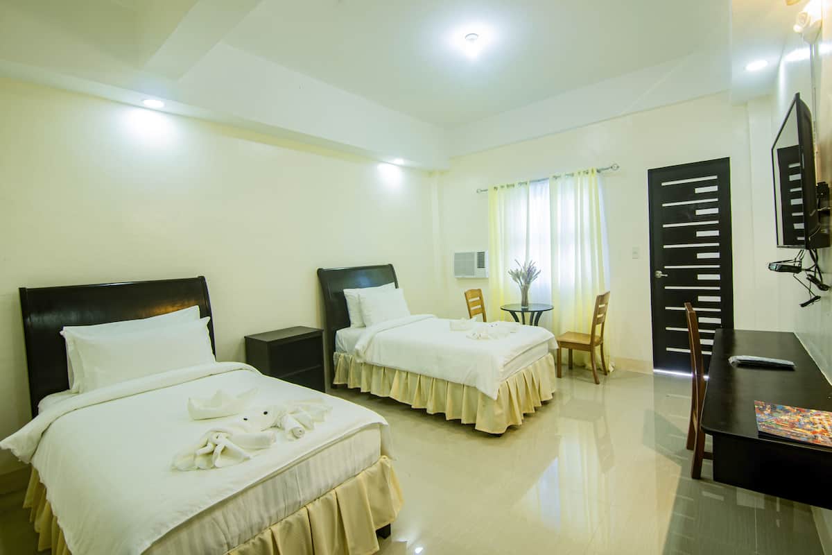 A hotel room with two beds, a desk, a chair, and a TV.