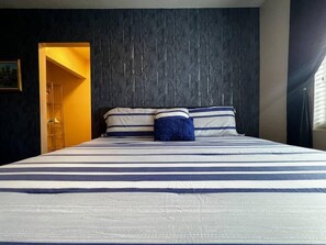A bed with striped bedding, a dark textured headboard, and a door leading to another room.