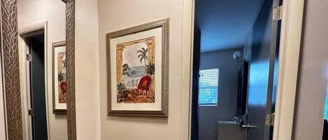 A hallway with a woven basket, framed artwork, and a door leading to a bathroom.