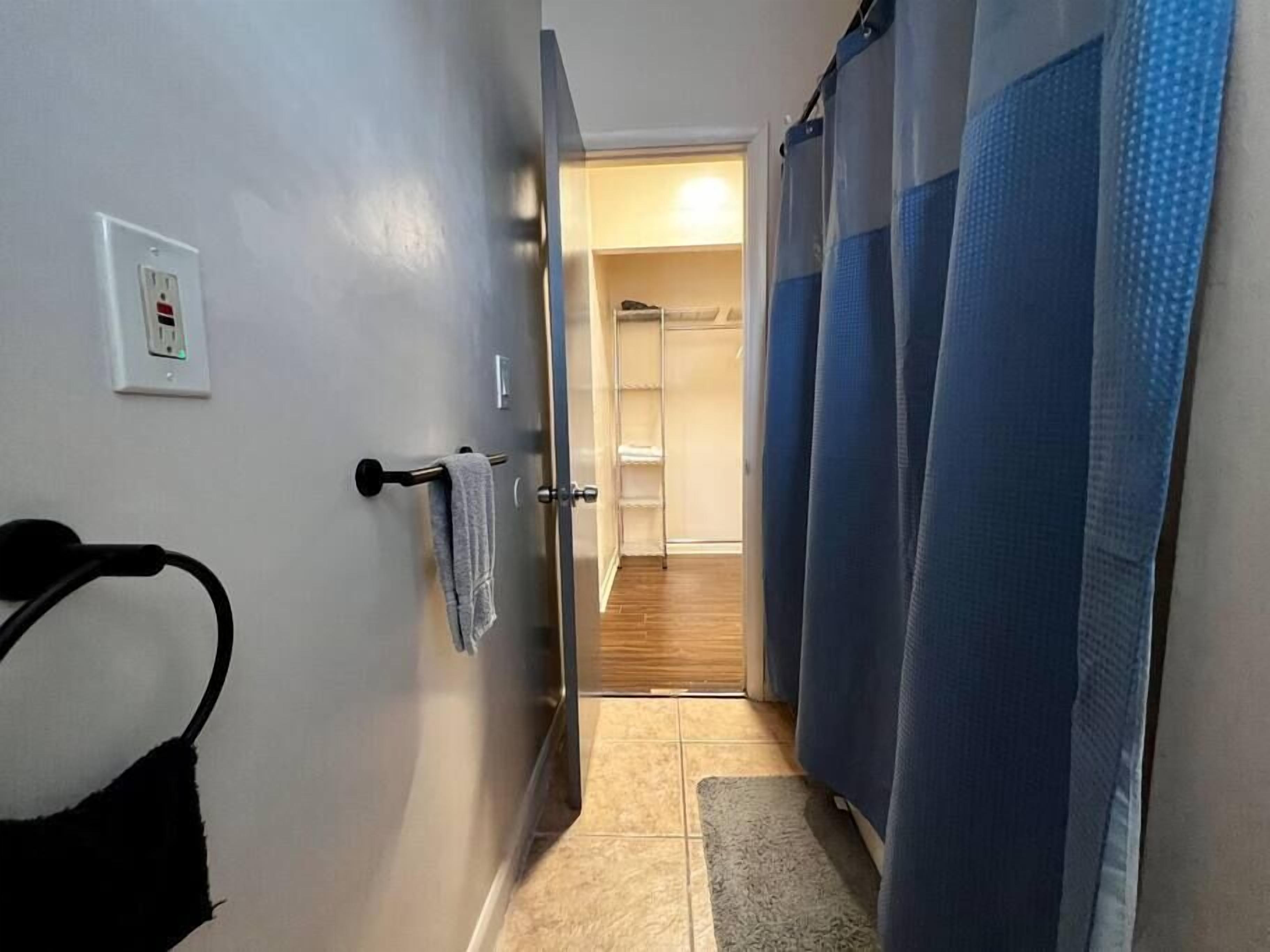 A narrow hallway with a towel rack, a power outlet, and a shower area with blue curtains.