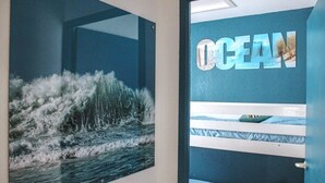 Een kamer met stapelbedden, een muur waarop 'OCEAN' staat en een groot schilderij met een zeethema.