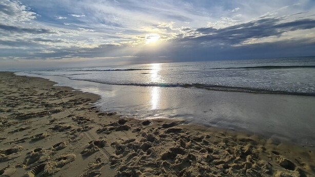 Een strand met voetafdrukken in het zand en de zon die ondergaat boven de oceaan.