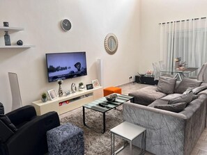 A modern living room with a flat-screen TV, a marble sofa, a glass coffee table, and a small side table. - Accra Cozy Retreat With 2 Bedrooms (Santeo)