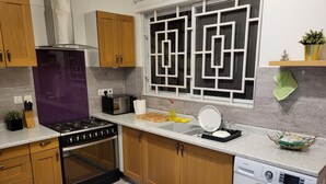 A modern kitchen with wooden cabinets, a gas stove, a microwave, and a built-in washing machine. - Accra Cozy Retreat With 2 Bedrooms (Santeo)