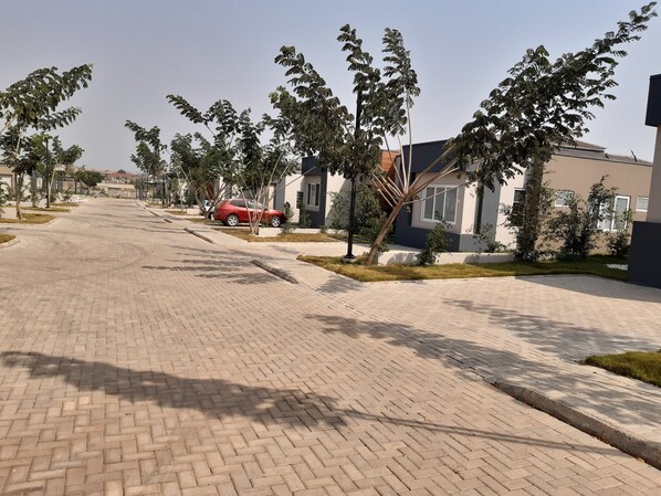 A paved walkway with trees and modern buildings. - Accra Cozy Retreat With 2 Bedrooms (Santeo)