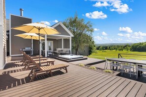 A wooden deck with outdoor furniture, a hot tub, and a view of a golf course.