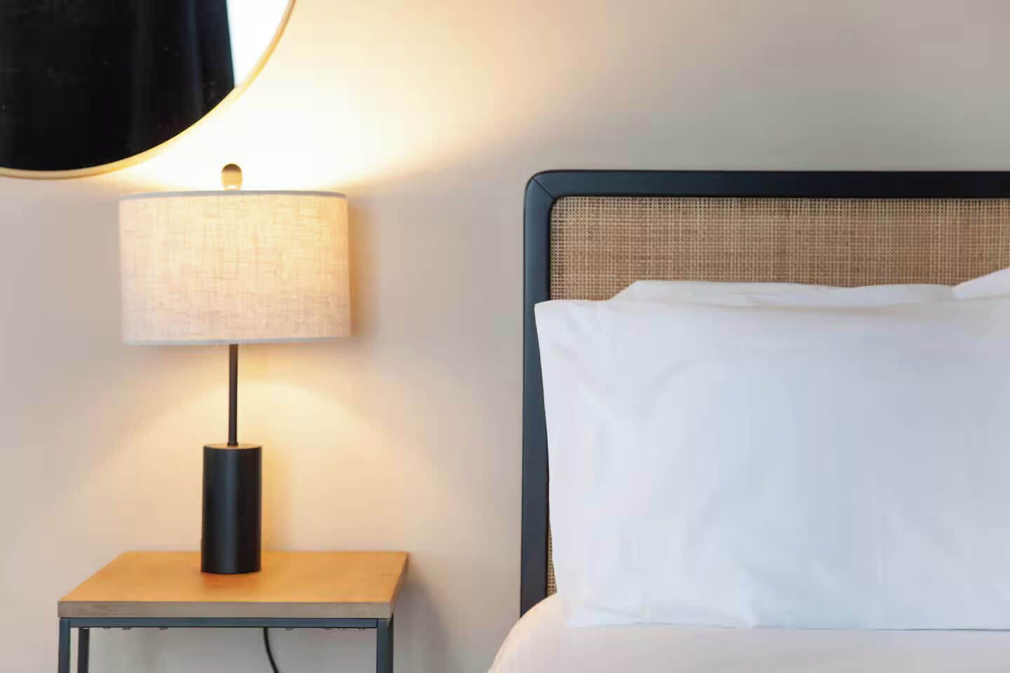 Un lit bien fait, avec du linge de lit blanc et une tête de lit à la texture tissée.