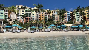 A beachfront hotel with multiple colorful buildings, clear blue water, and rows of sun loungers under blue umbrellas. - FULL RESORT ACCESS! Marriott Two Bedroom Suites with full kitchen (St Thomas)