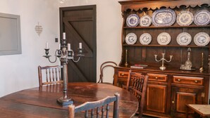 A dining room with a wooden table, chairs, a chandelier, and a china cabinet with plates. - Sea Chest (Conwy)