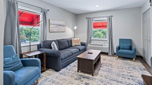 Un salon moderne avec un canapé gris, des fauteuils bleus, une table basse en bois et un tapis à motifs.