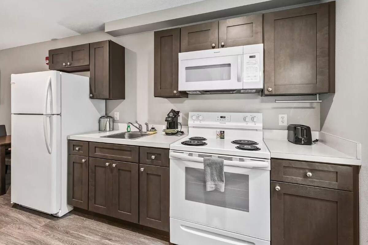 A modern kitchen with a refrigerator, microwave, stove, and dark wooden cabinets.