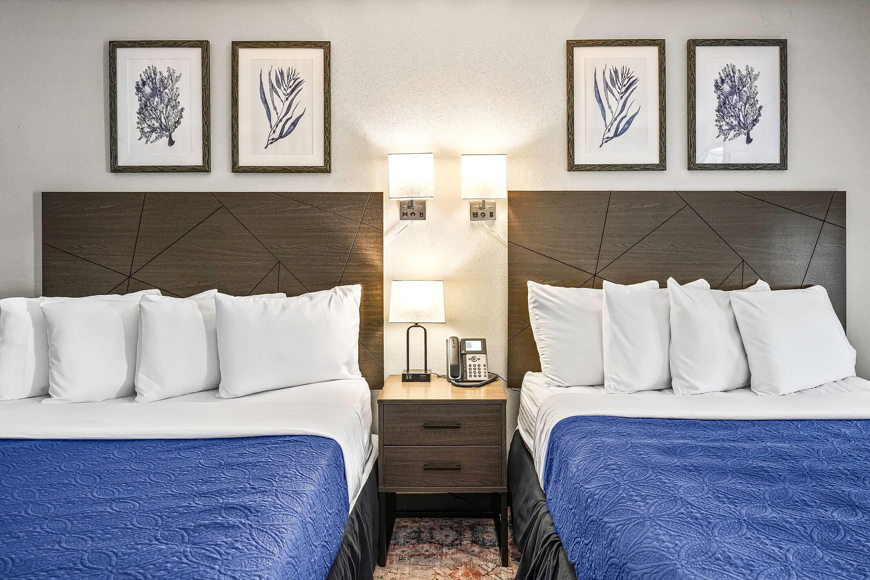 A hotel room with two beds, a nightstand with a phone, and wall-mounted artwork.