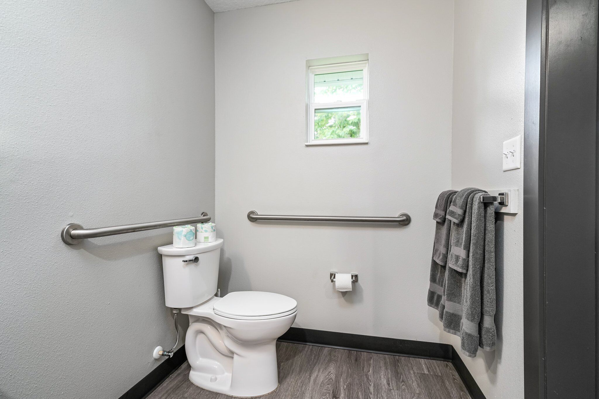 Une petite salle de bain individuelle, avec des toilettes blanches, une fenêtre et un porte-serviettes.