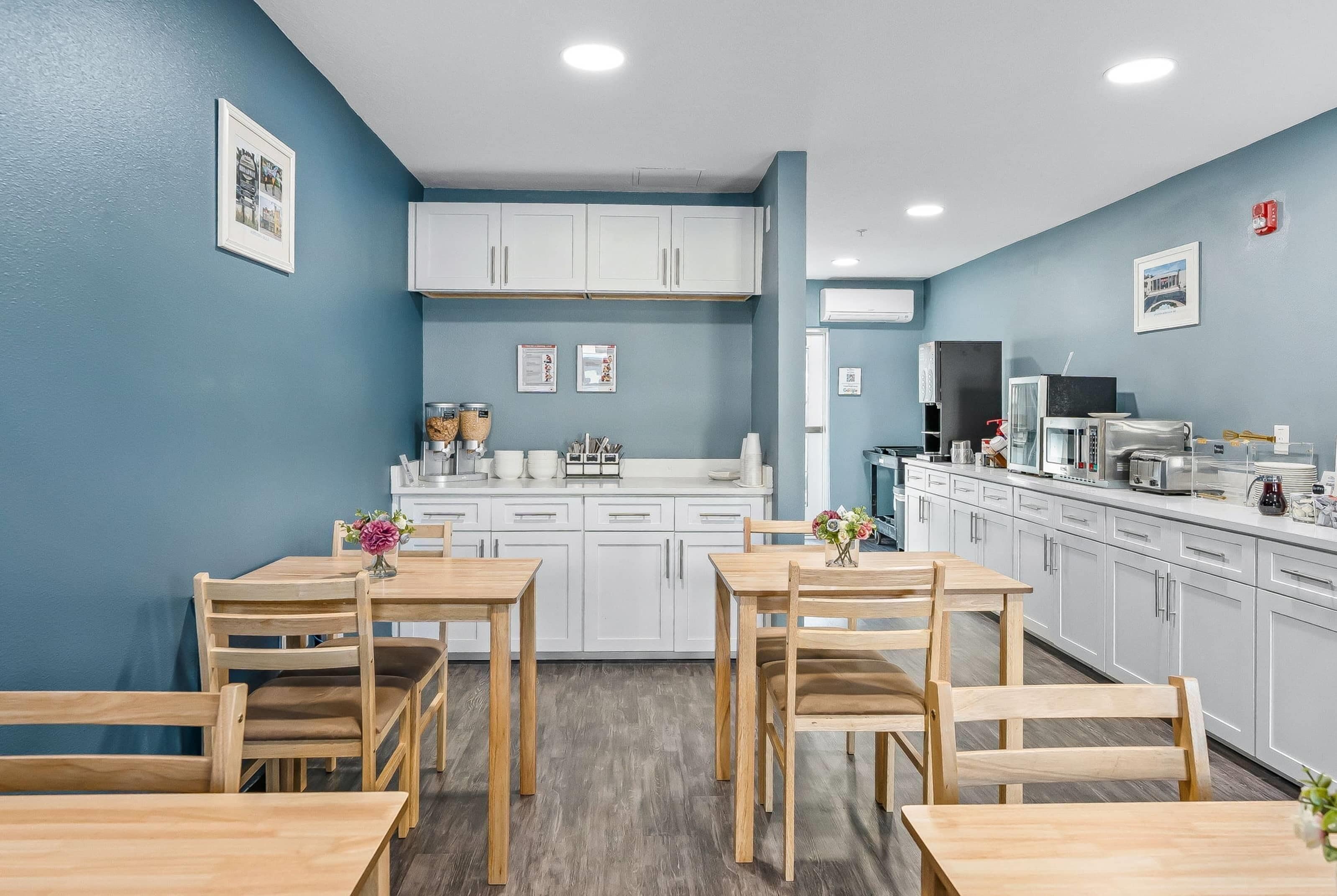 Een moderne keuken met witte kasten, een centraal eiland en een eethoek met houten tafels en stoelen.