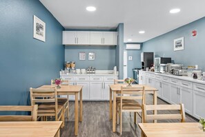 Une cuisine moderne avec des meubles blancs, un îlot central et un coin repas doté de tables et de chaises en bois.