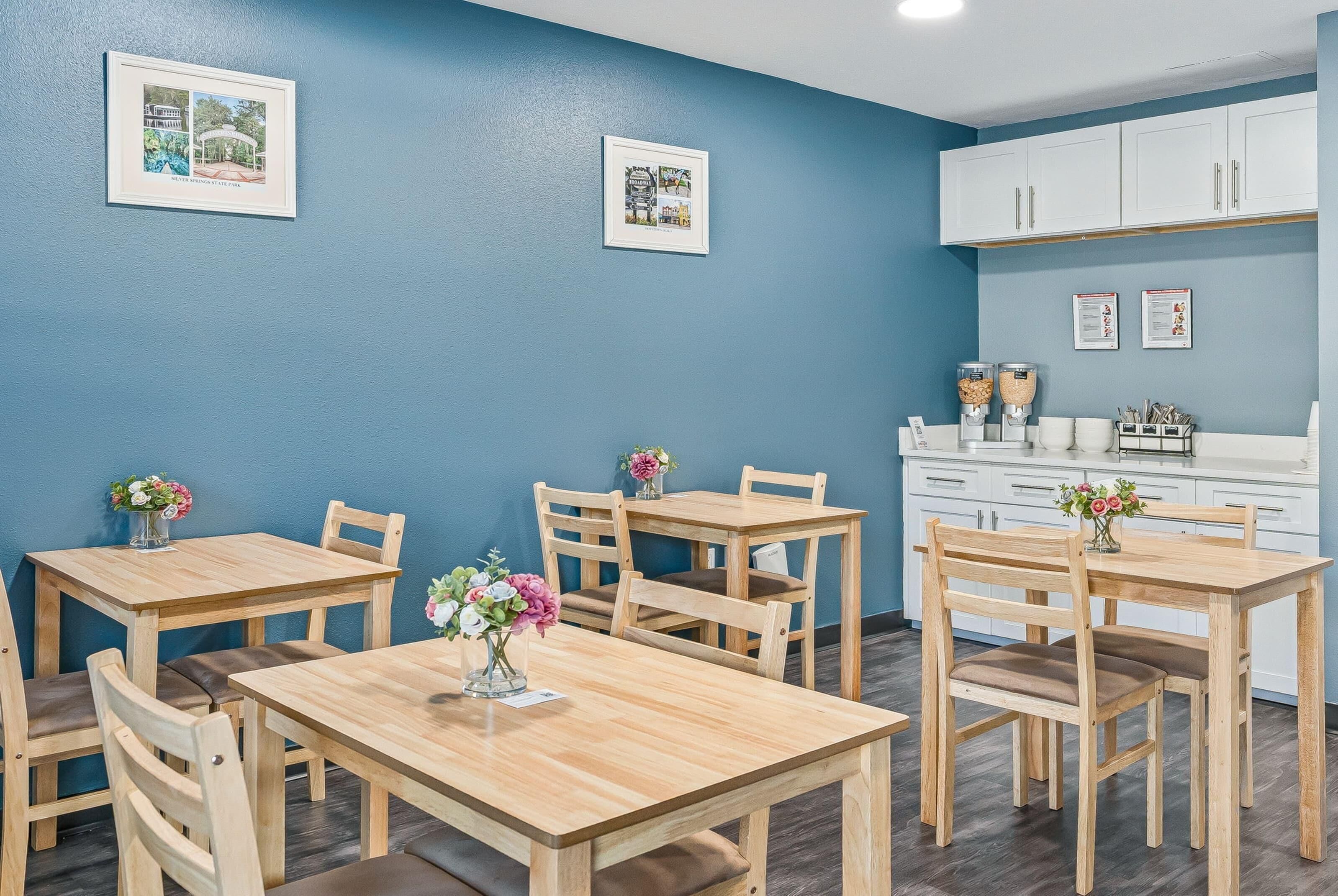 A dining area with wooden tables and chairs, a coffee machine, and framed pictures on the wall.