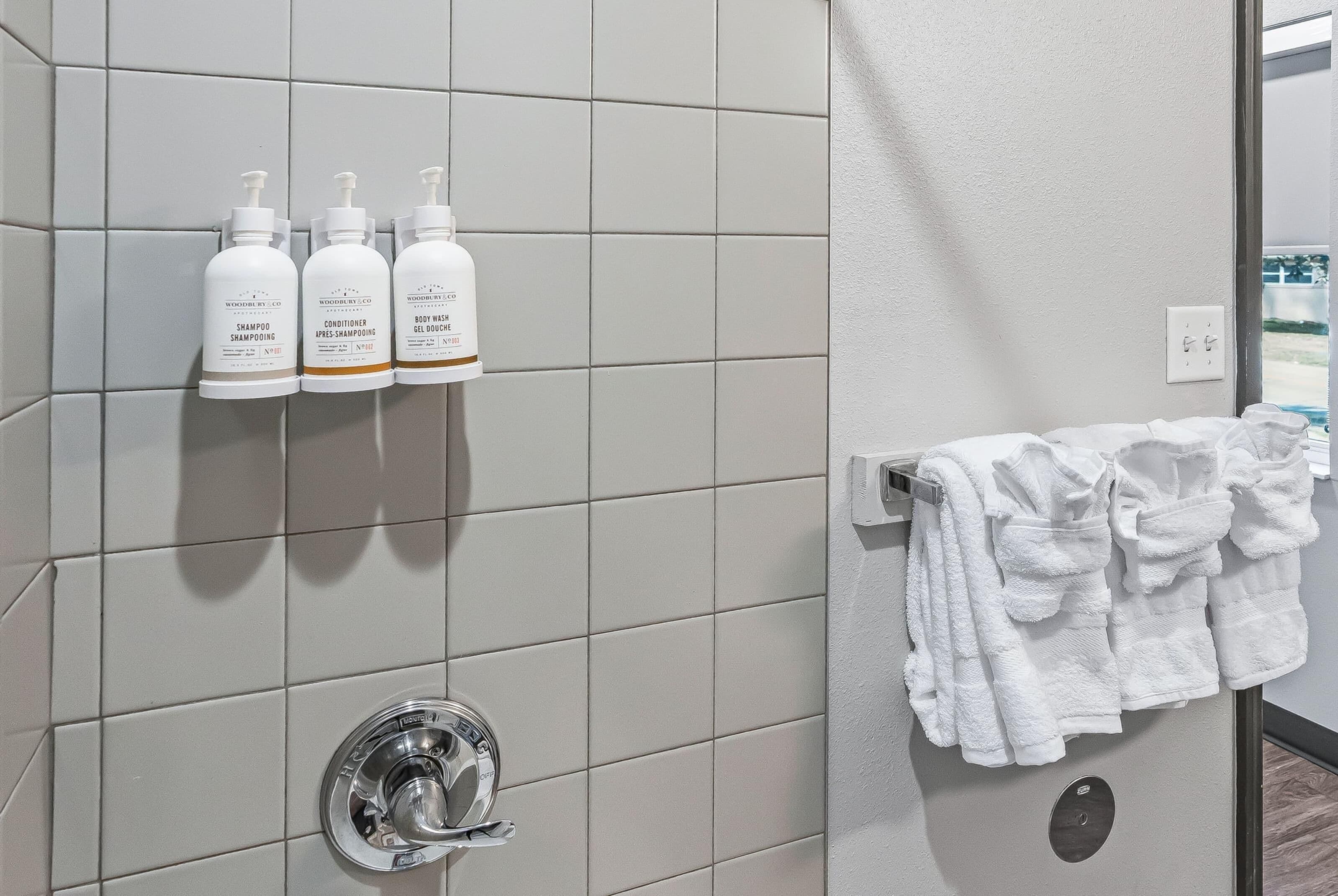 A bathroom with white tiles, a towel rack with towels, and three bottles of toiletries on the wall.