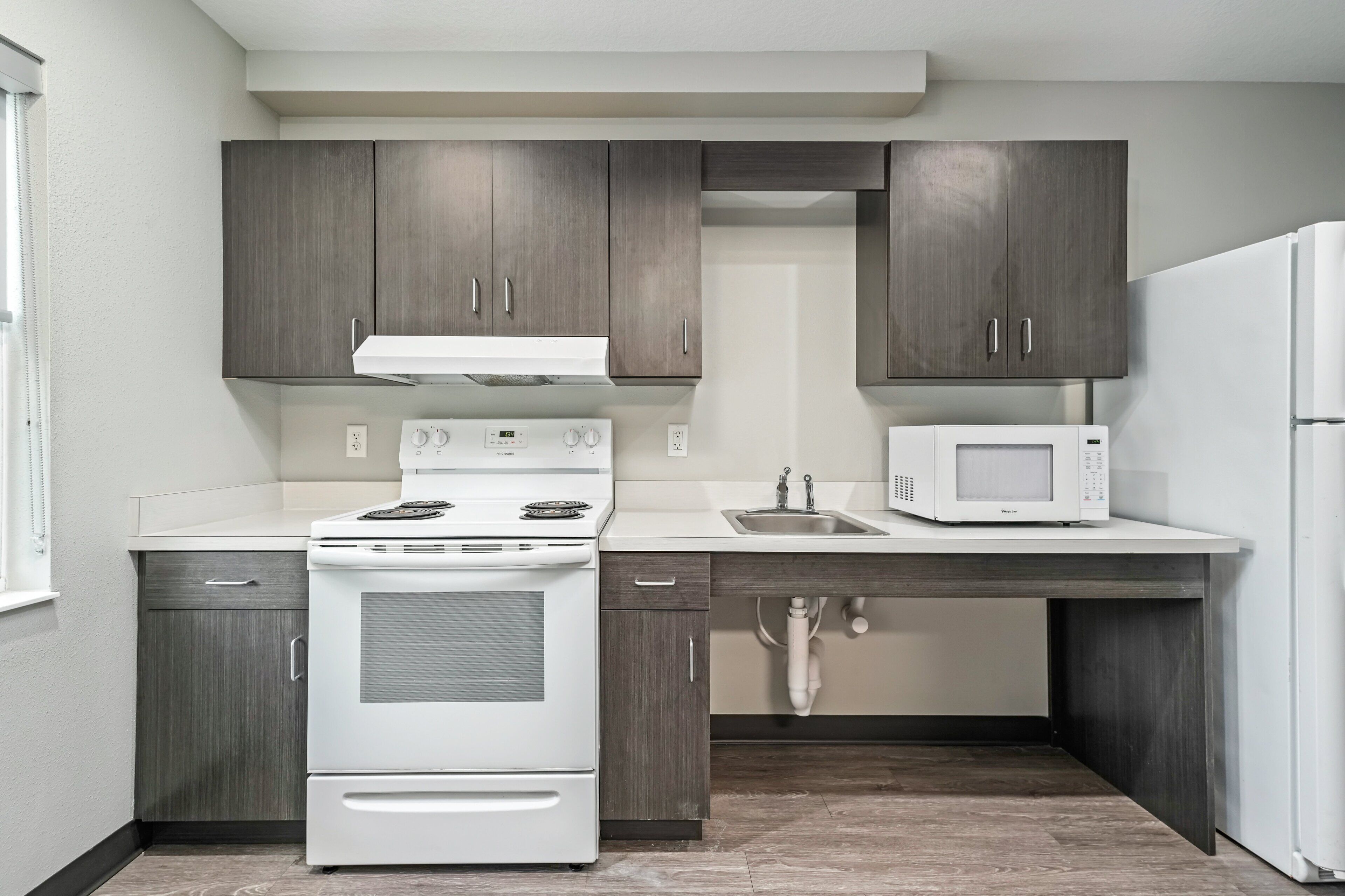 A compact kitchen with dark wood cabinets, a white stove, a microwave, and a sink.