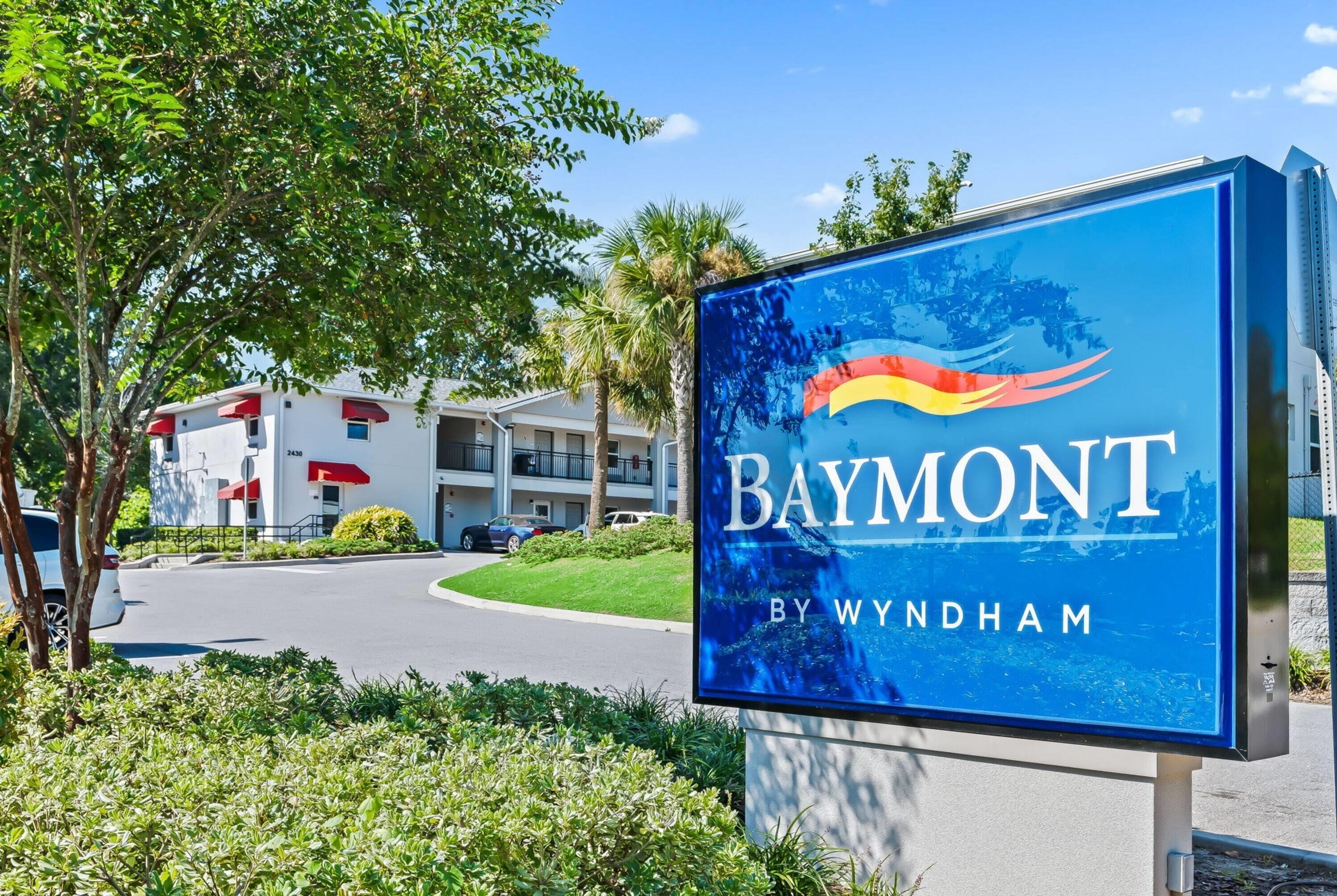 A sign for Baymont by Wyndham with a clear view of the surrounding area including a road, a building, and some greenery.