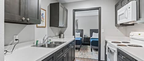 Une cuisine moderne avec des meubles sombres, un plan de travail blanc, un four à micro-ondes encastré et une cuisinière. On y trouve également un petit coin repas avec une table et des chaises.