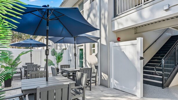 En patio med udendørs møbler og parasoller, et hvidt gelænder samt en trappe op til en etage.