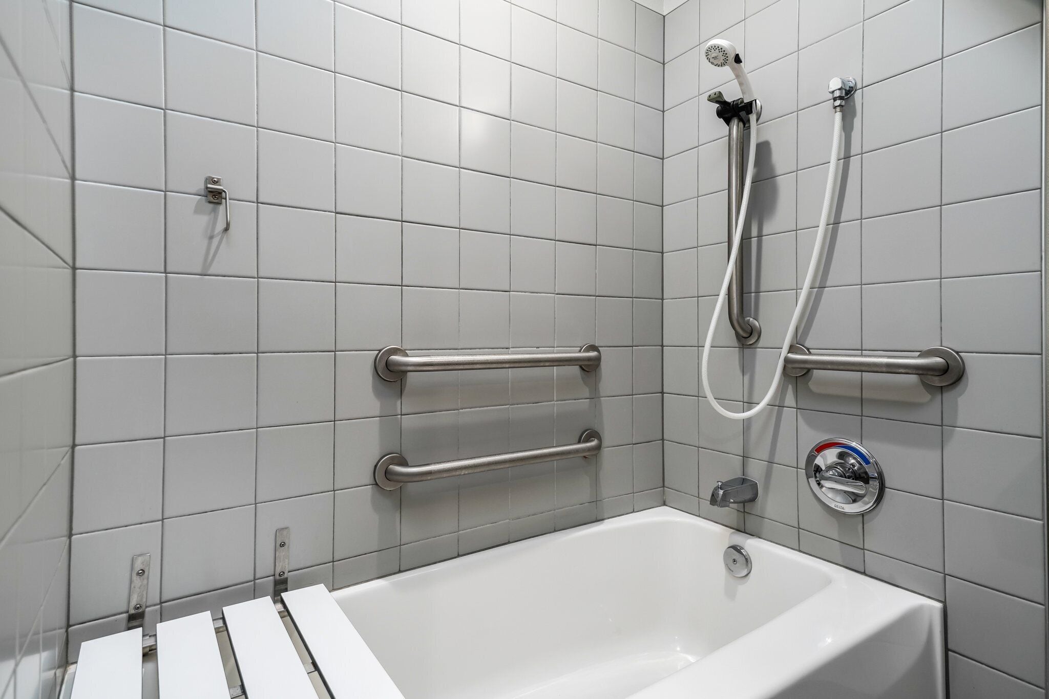 Une salle de bain moderne avec des carreaux blancs, une baignoire et des barres d’appui pour plus de sécurité.