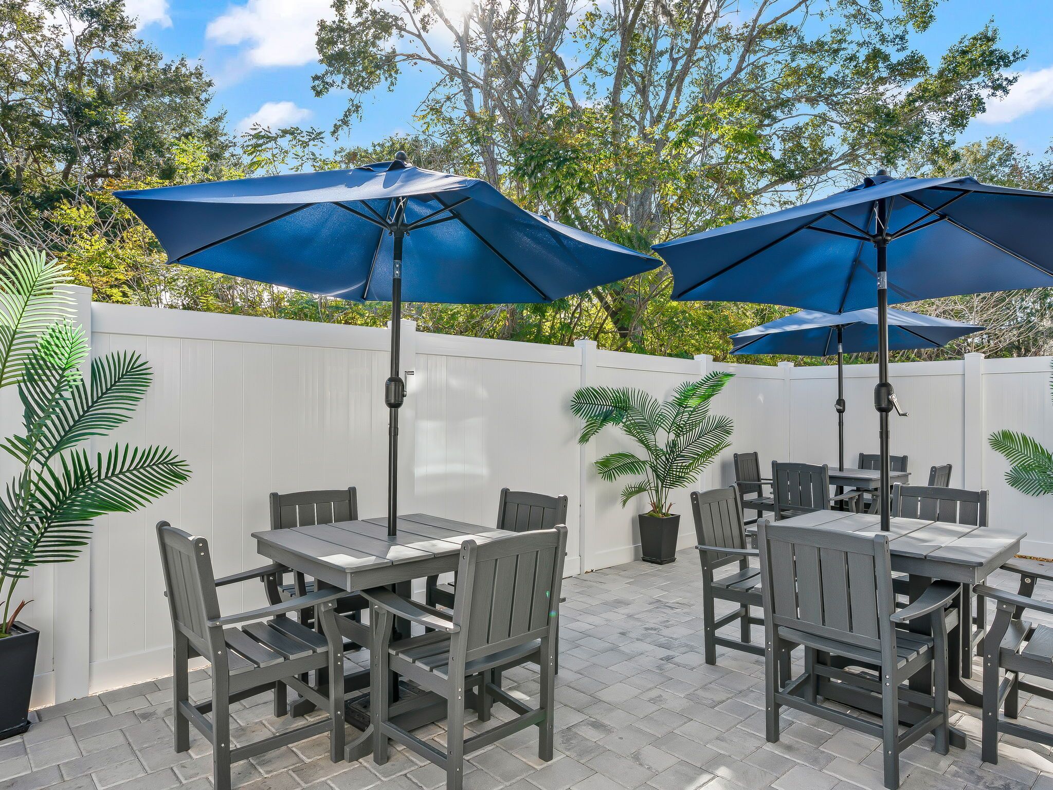 Eine Terrasse mit Tischen, Stühlen, blauen Sonnenschirmen und Topfpflanzen.