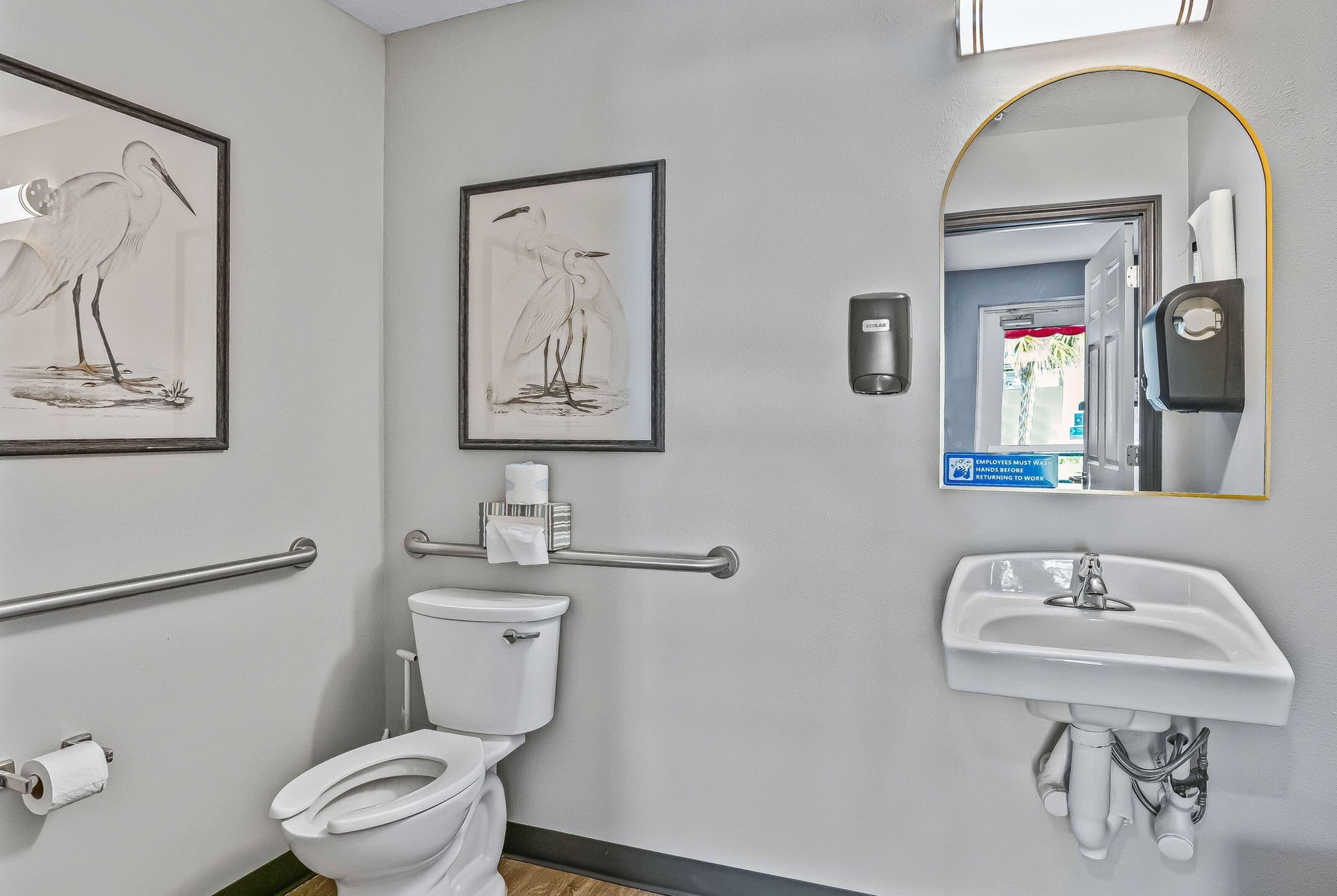 A modern bathroom with a toilet, bidet, hand dryer, and framed wall art.