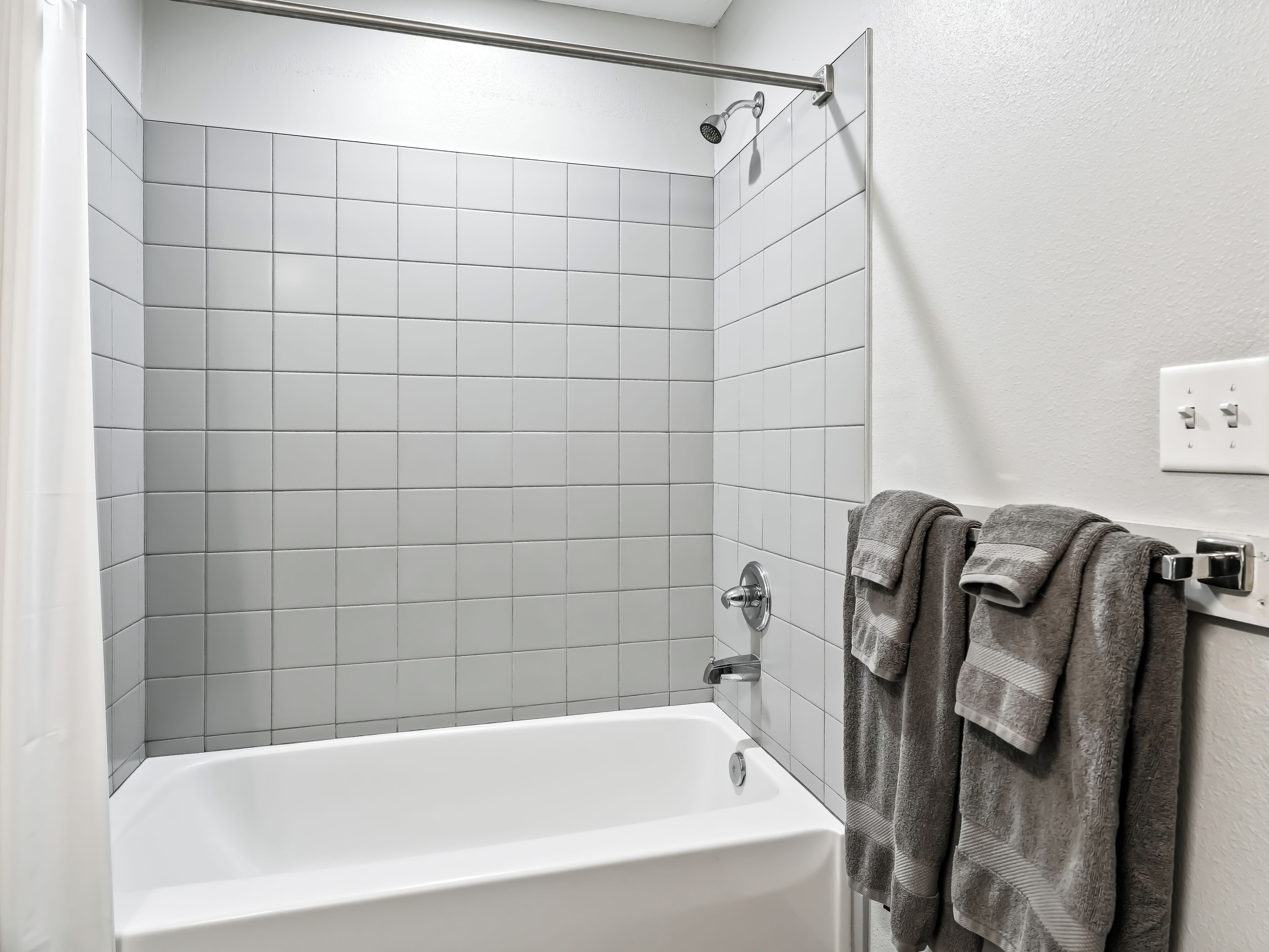 Un baño con una bañera blanca, una ducha con cabezal de ducha manual y un perchero con dos toallas.