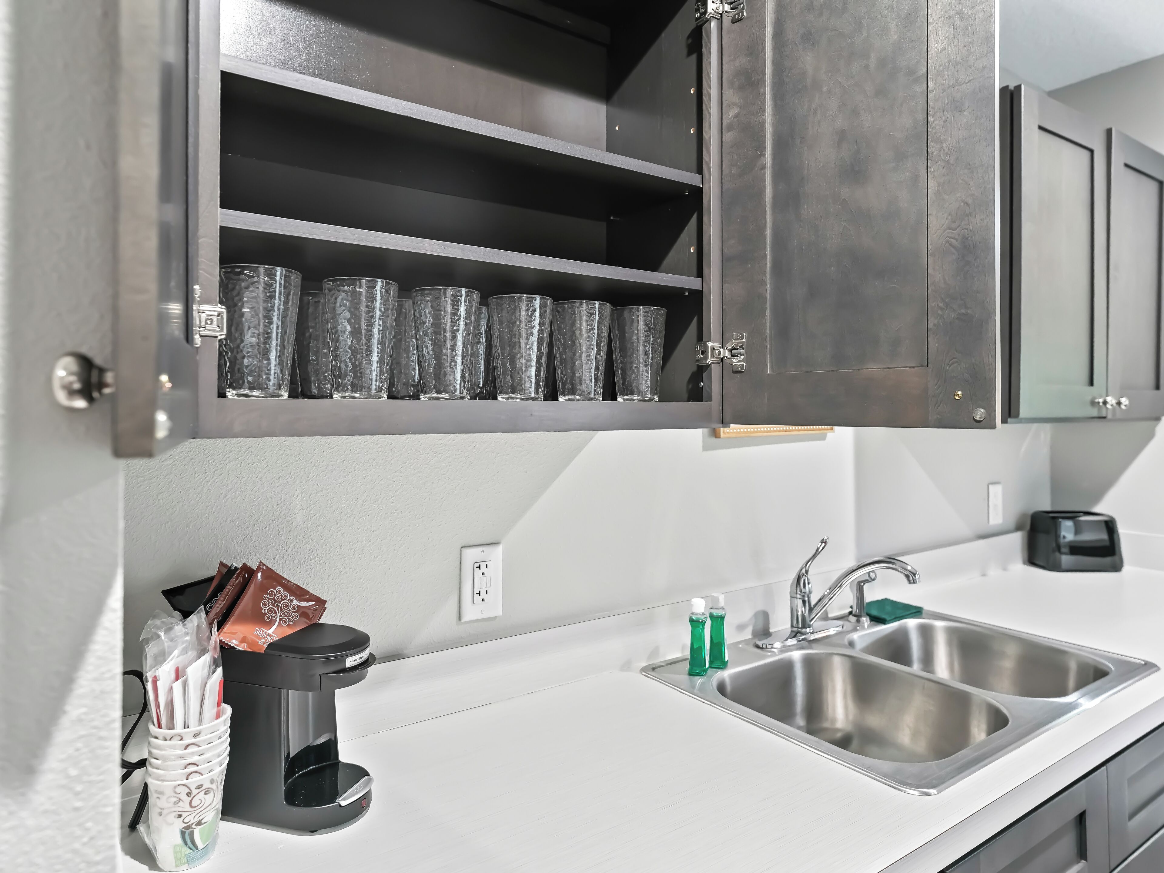 A modern kitchen with a built-in coffee maker, a double sink, and a shelf with glasses.