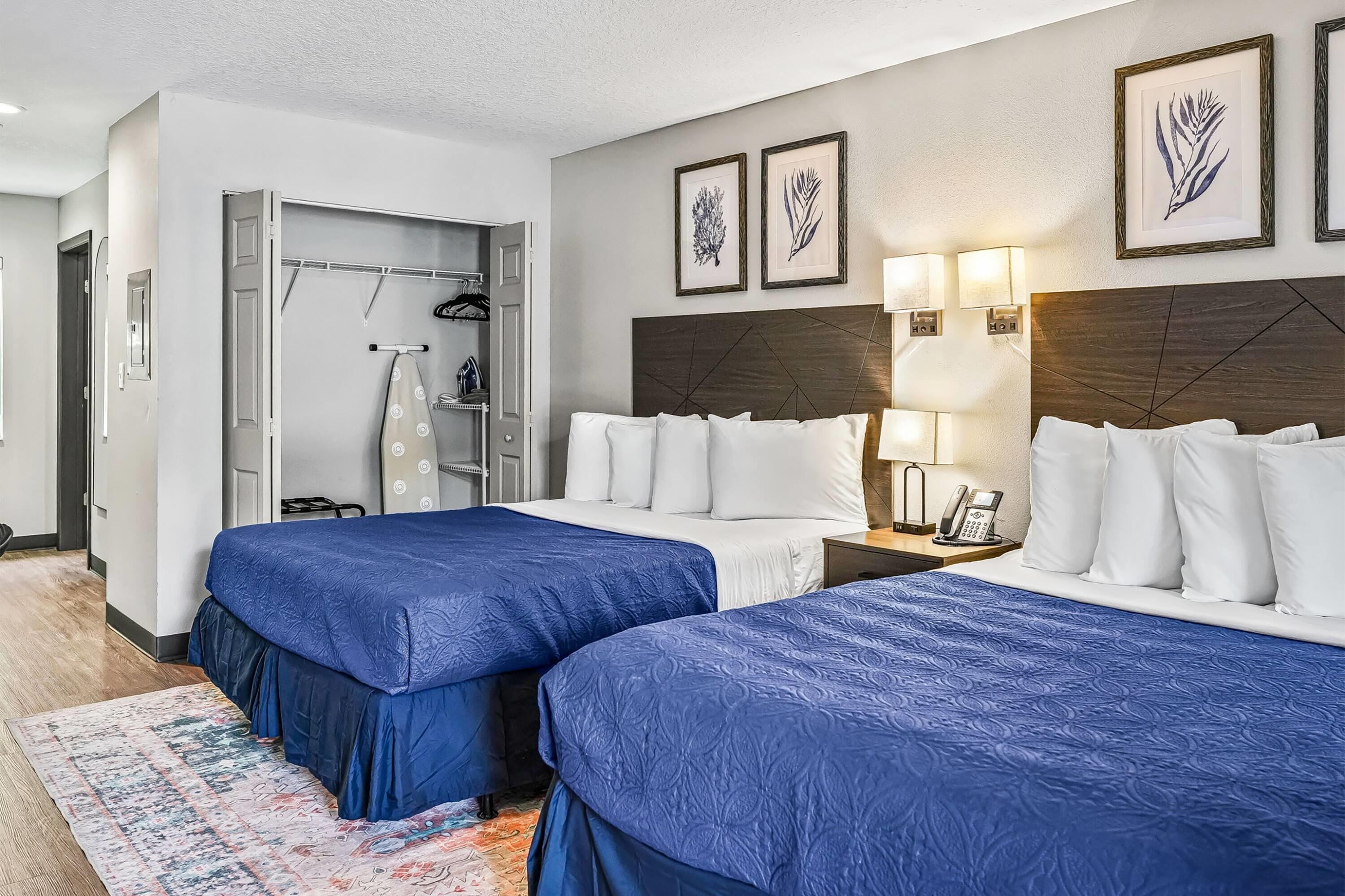 A hotel room with two beds, a wardrobe, a shower, and framed artwork on the wall.