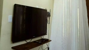 A flat-screen TV mounted on a wall with a wooden shelf below. - Chalés Pôr do Sol Gostoso (São Miguel do Gostoso)