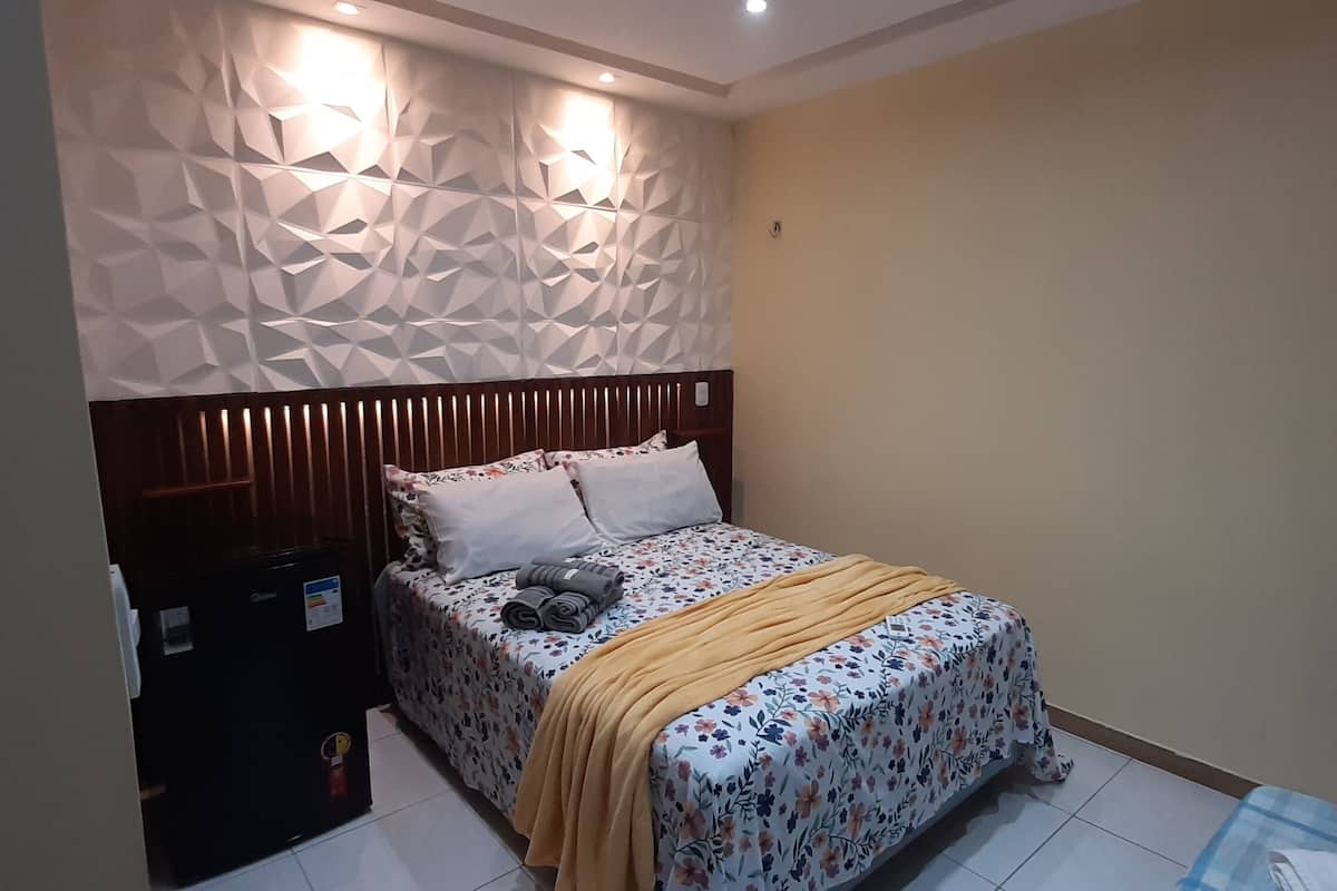 Ein Schlafzimmer mit einem Bett, einem Nachttisch, einer Wandleuchte und einer Wand mit geometrischem Muster.