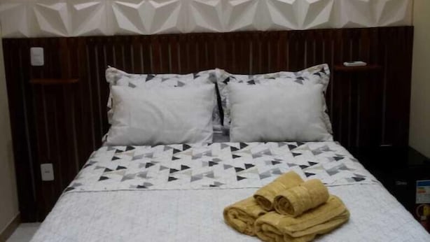 A neatly made bed with a geometric-patterned headboard, a folded towel on the bed, and a dark wooden nightstand beside it. - Chalés Pôr do Sol Gostoso (São Miguel do Gostoso)