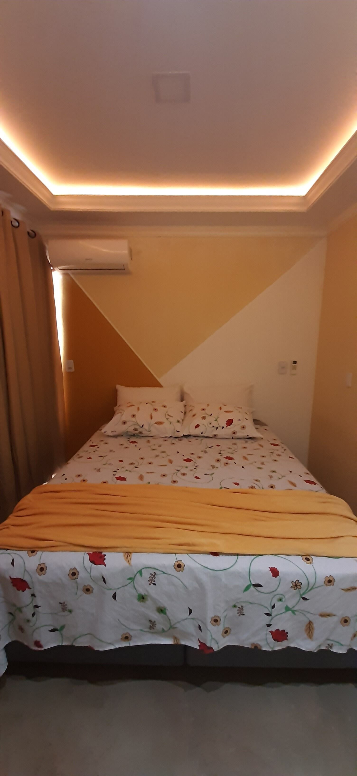 A bedroom with a bed, floral bedspread, and a ceiling light fixture.