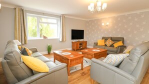 A living room with two grey sofas, a wooden coffee table, a TV, and a wall-mounted light fixture. - Fallowfield (Great Yarmouth)