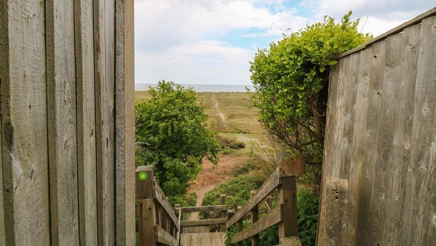 A wooden staircase leading to a scenic overlook with a view of the sea and distant hills. - Fallowfield (Great Yarmouth)