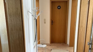 Käytävä, jossa on puulattia, naulakko, valkoinen tuoli ja matto.