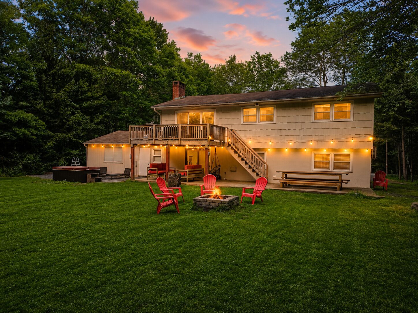 A two-story house with a deck, outdoor seating, and a fire pit.