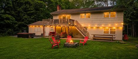 A two-story house with a deck, outdoor seating, and a fire pit.