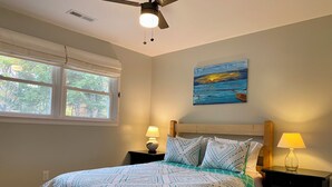 Un dormitorio con una cama, dos mesitas de noche, un ventilador de techo, una ventana y un cuadro en la pared.