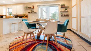 A modern kitchen with white cabinets, a dining area with a colorful rug, and a large window with blinds. - Stylish and funky, minutes away from everything NWA has to offer! (Springdale)