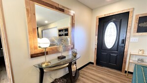 A hallway with a wooden-framed mirror, a glass console table with a light, and a black door with a window. - Stylish and funky, minutes away from everything NWA has to offer! (Springdale)