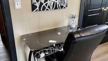 A modern office space with a glass desk, black leather office chair, and a wall-mounted floral artwork.