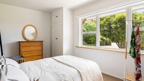 A bedroom with a bed, dresser, and window with a view of greenery. - Emily's Beach House - Kaiteriteri Holiday Home (Kaiteriteri)