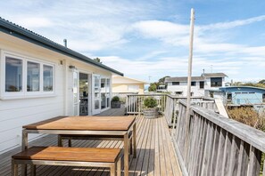 Terraza de madera con una mesa y sillas, con vistas a una zona residencial que incluye casas y una piscina.